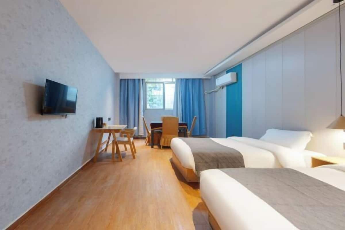 Una habitación de hotel con cama, escritorio, silla, televisor y ventana con cortinas.