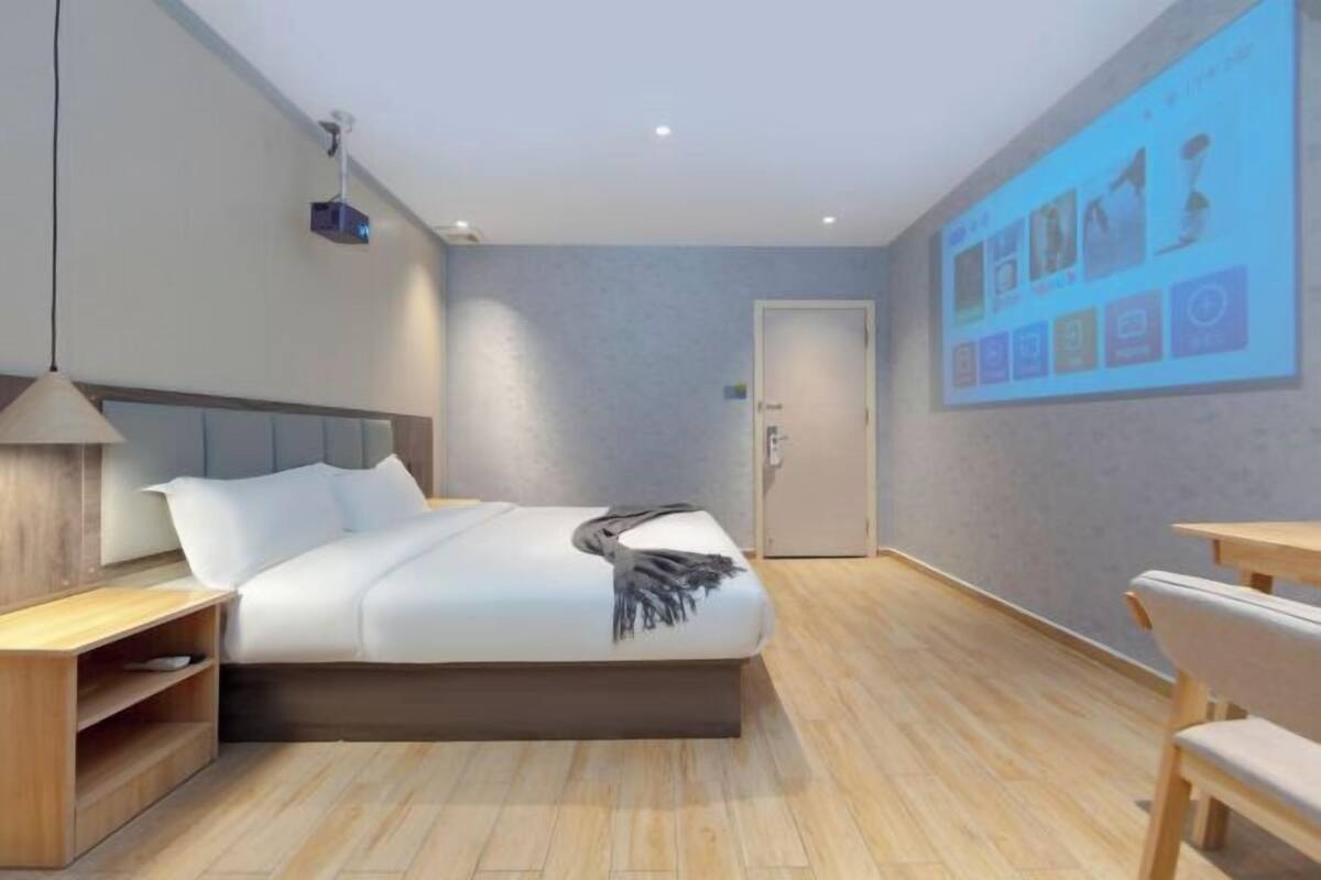 Una habitación de hotel moderna con una cama, una mesita de noche y un proyector de pared mostrando una presentación.