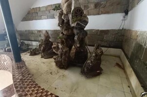 Una habitación con pared de piedra, una estructura de madera que recuerda a un árbol y suelo de baldosas.