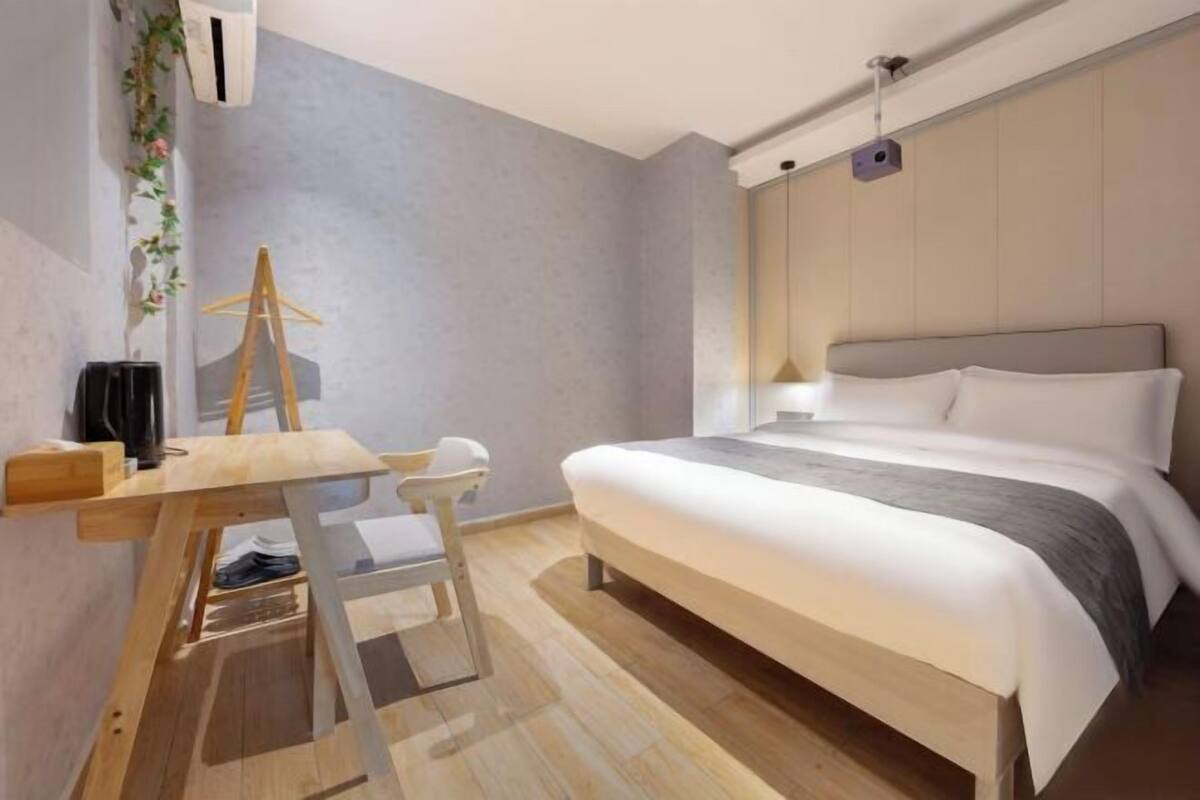 Un dormitorio con cama, mesita de noche, silla y escritorio con planta colgante.