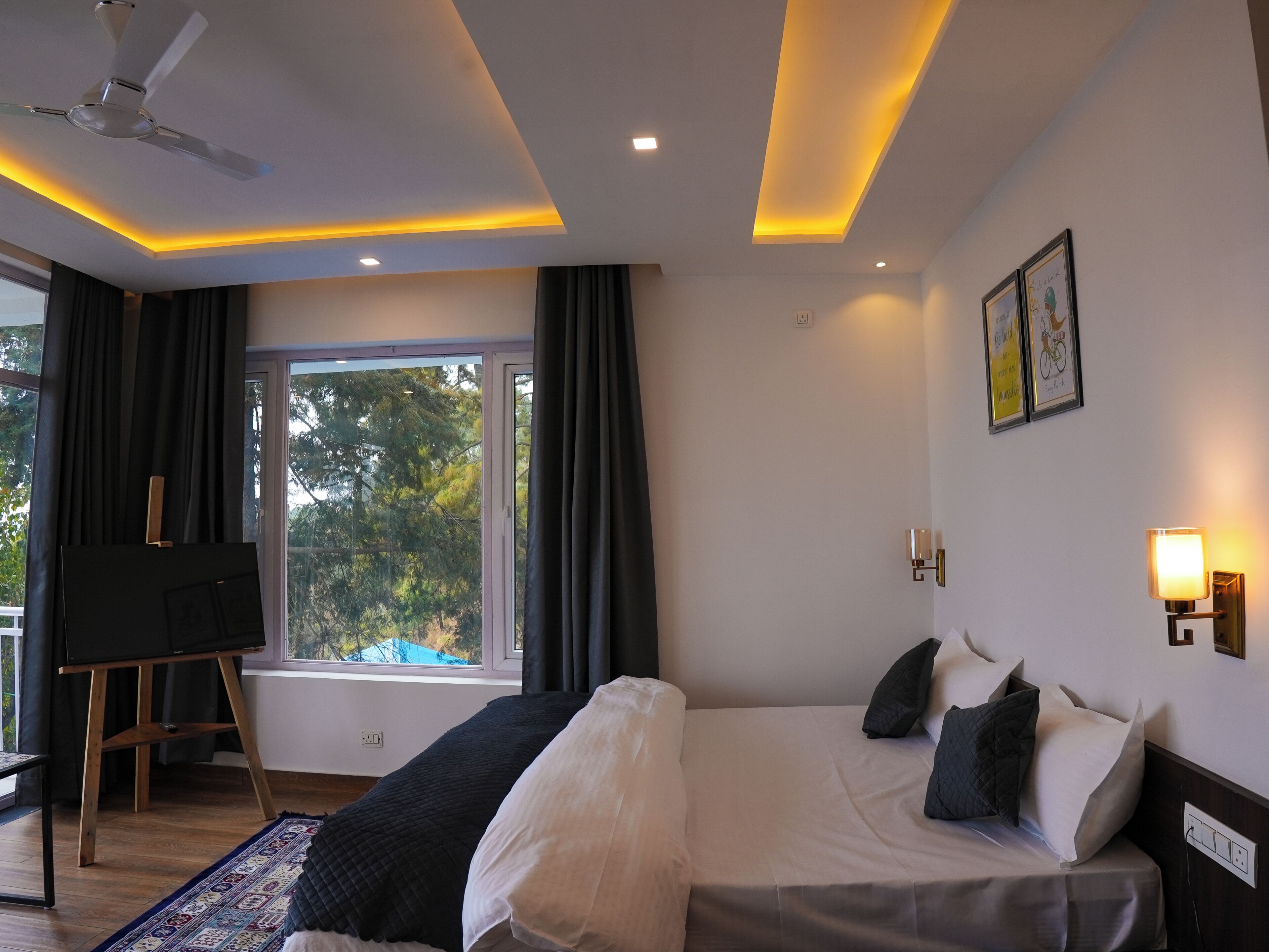 A modern hotel room with a large bed, a desk, a standing fan, and a window with curtains.