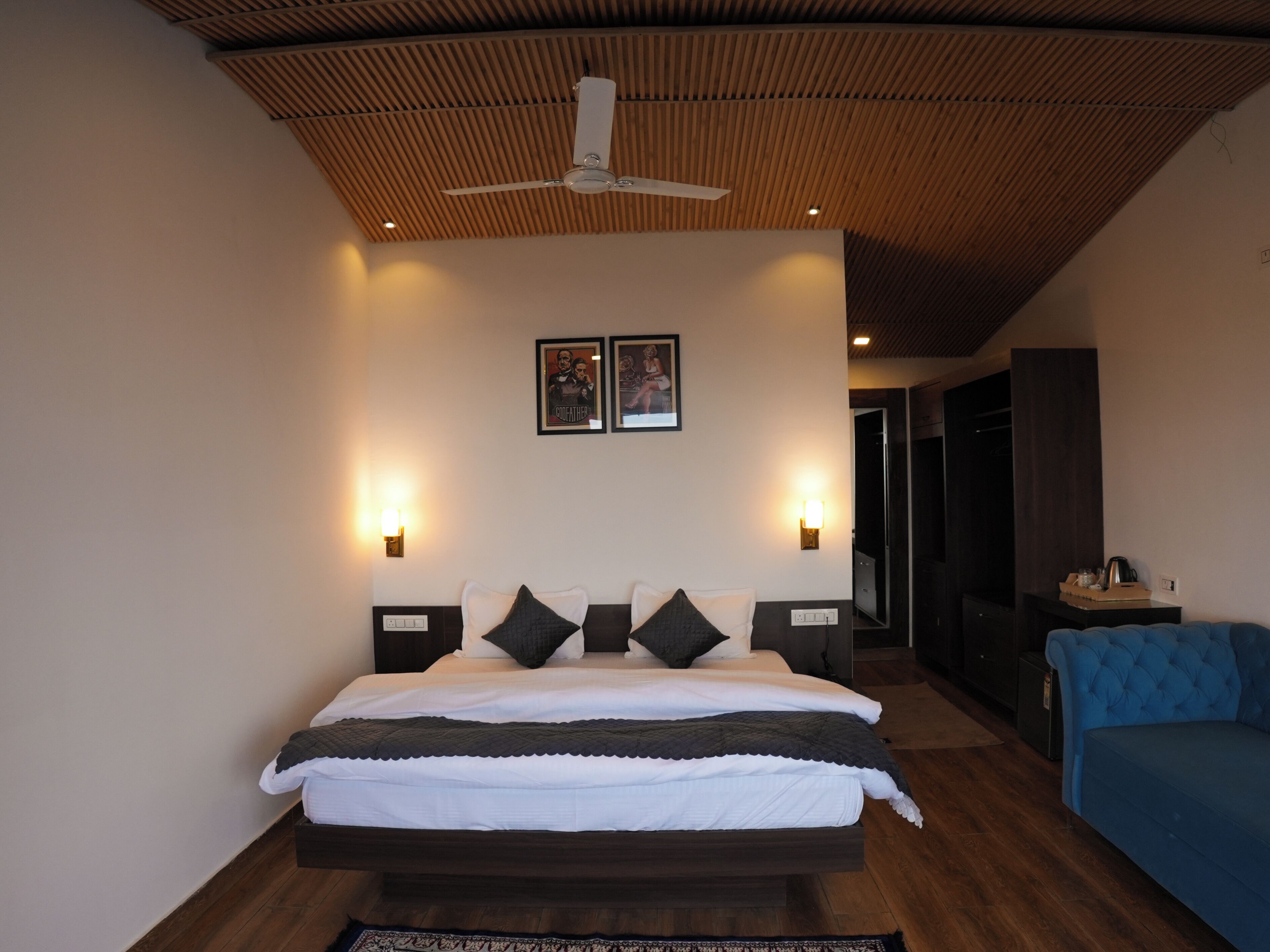 A bedroom with a bed, bedside tables, a ceiling fan, wall-mounted lights, and a blue sofa.