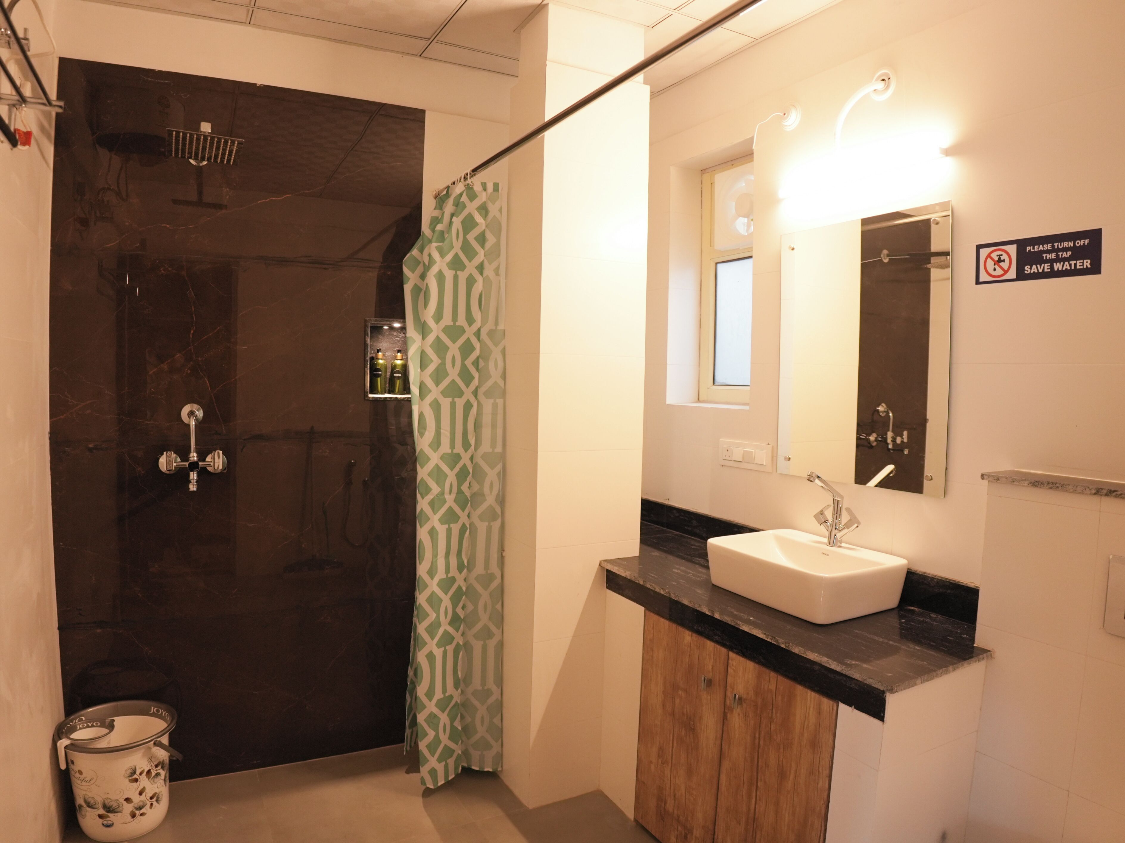 A bathroom with a shower, a sink, a mirror, and a sign advising to turn off the tap to save water.