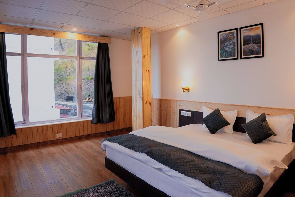 Hotellihuone, jossa on suuri sänky, puupanelointi, kattotuuletin ja kaksi kehystettyä kuvaa seinällä.