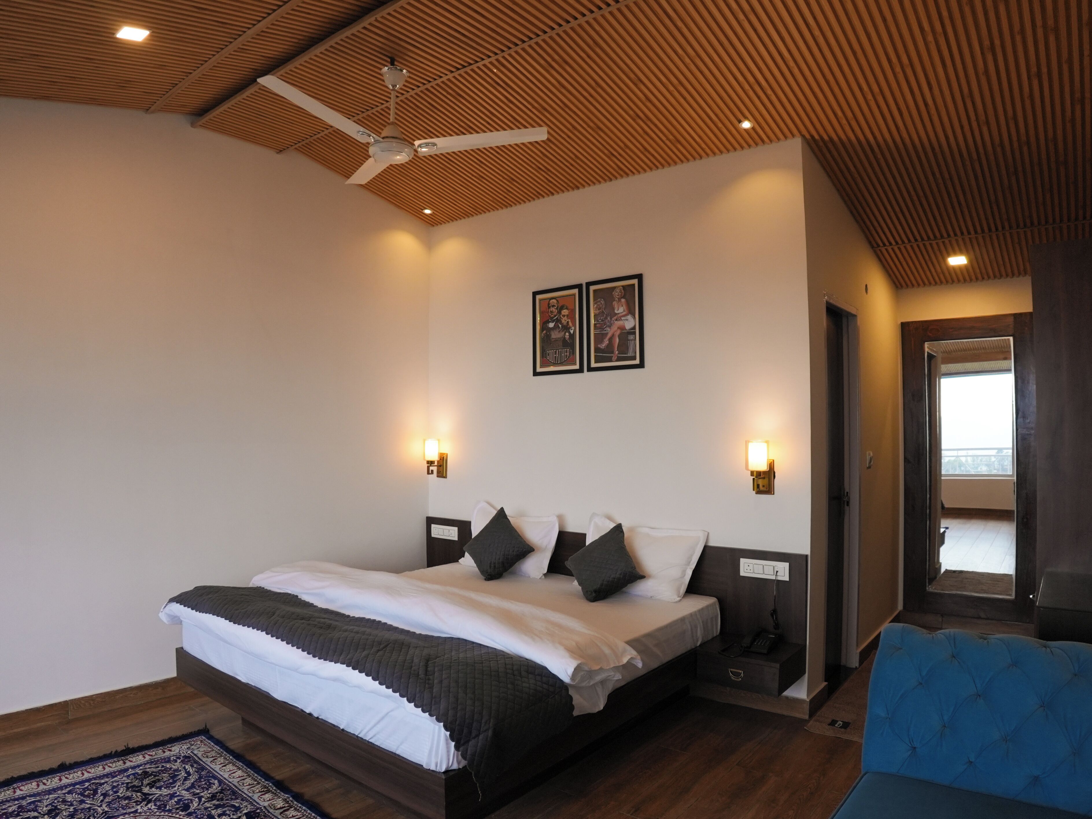 A modern bedroom with a large bed, wooden ceiling, two wall-mounted lights, and a ceiling fan.