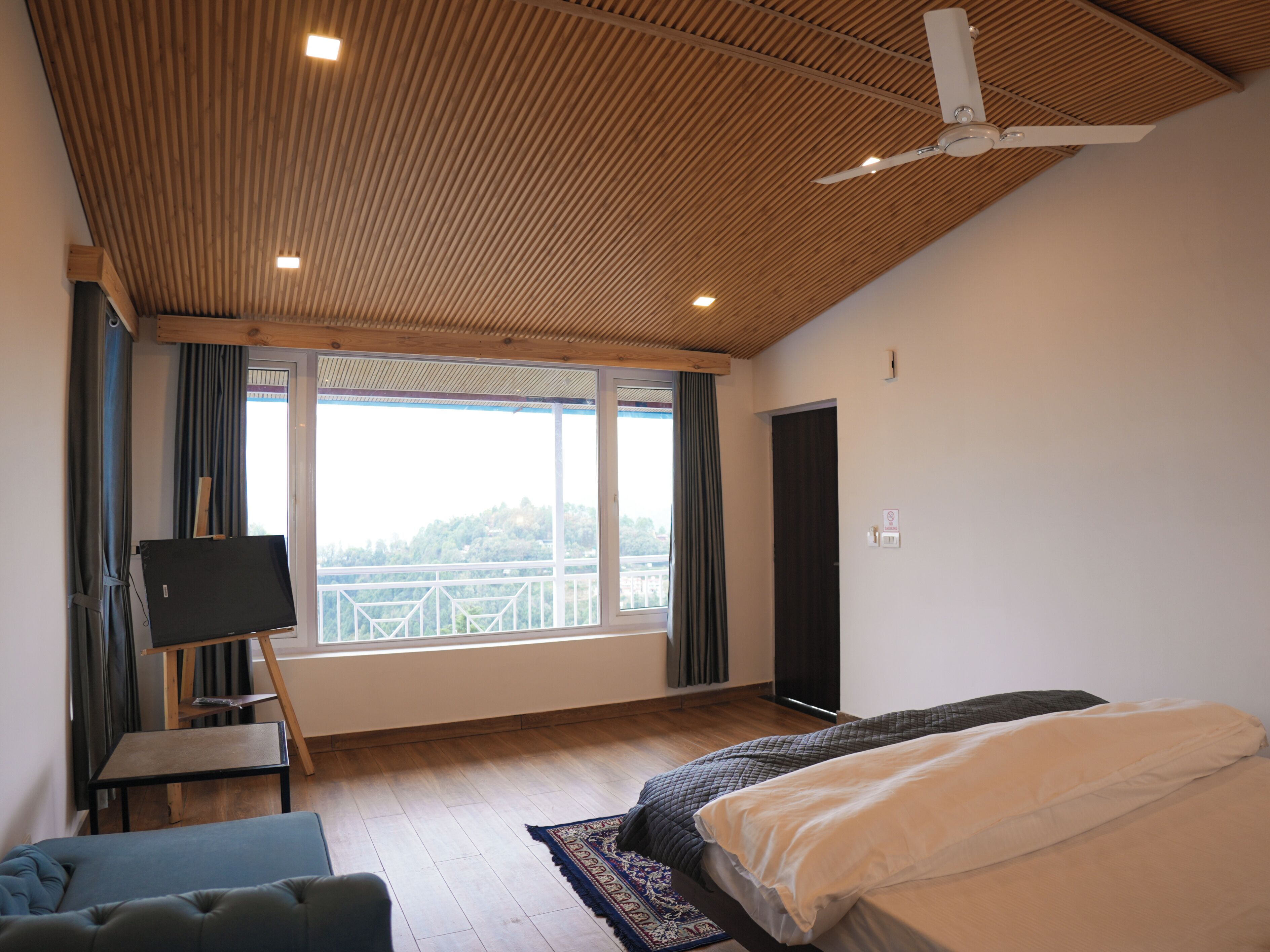 Un dormitorio con un ventanal grande, ventilador de techo y cama.
