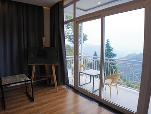 A room with a large sliding glass door leading to a balcony with a view of a mountainous landscape. - The Glass House Gethia (Nainital)