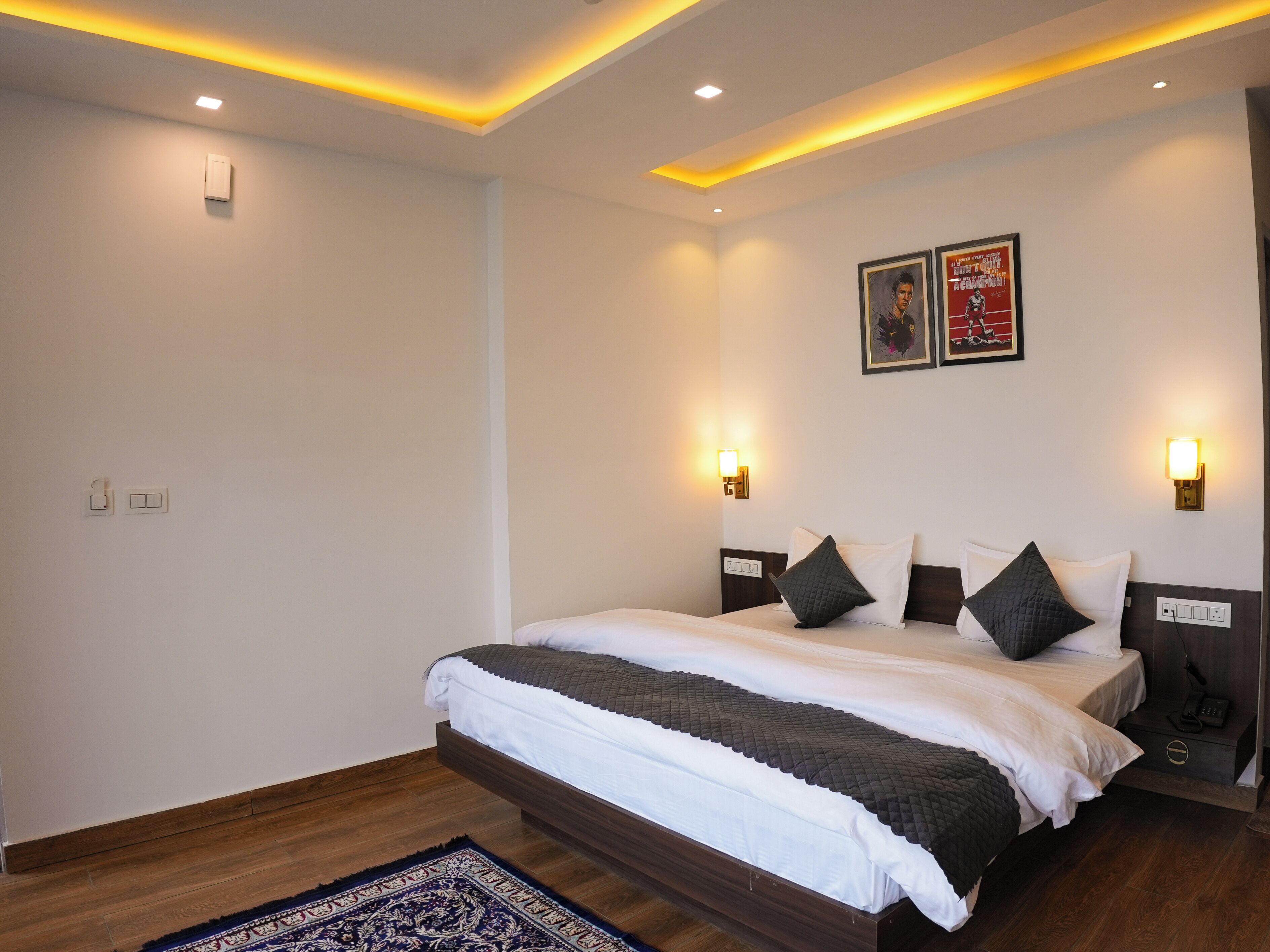A modern hotel room with a large bed, a wooden headboard, two wall-mounted lights, and a small nightstand.