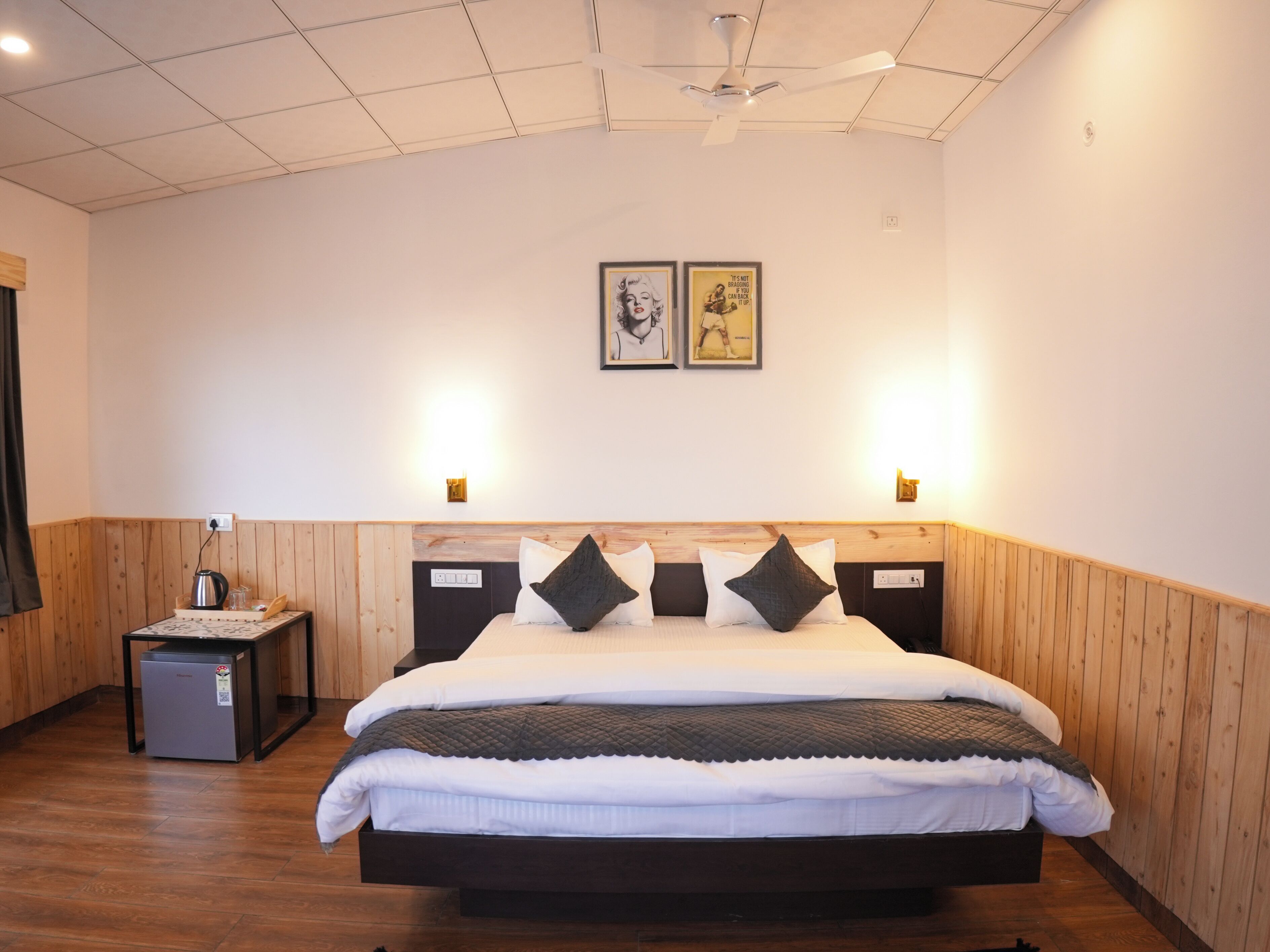 A bedroom with a large bed, wooden paneling on the walls, a ceiling fan, and two wall-mounted light fixtures.