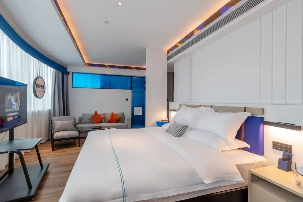 A modern hotel room with a large bed, a television, a desk, and a chair.