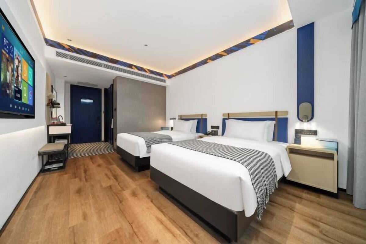 A hotel room with two beds, a desk, a chair, a TV, and a bathroom door.