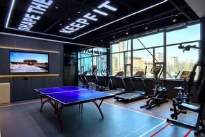 A gym with exercise equipment, a ping pong table, and a TV screen. - Mandu Hotel (Weifang)