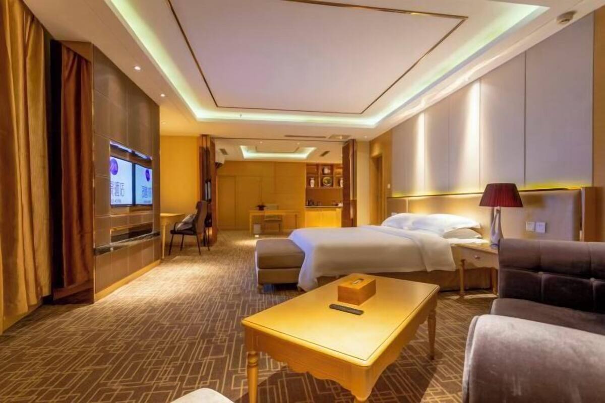 A hotel room with a bed, a desk, a chair, a sofa, a TV, and a minibar.