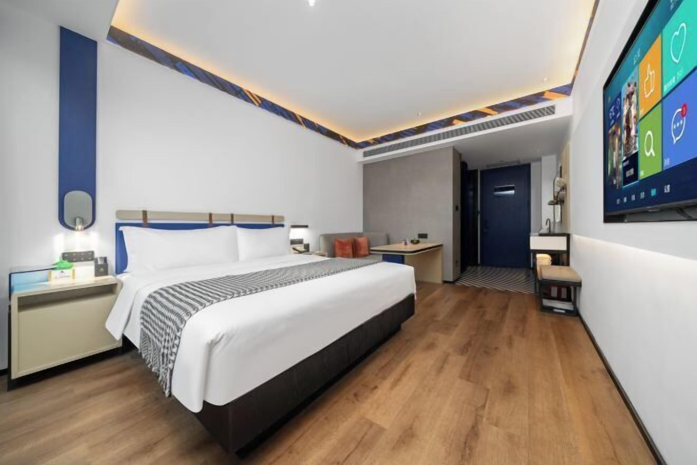 A modern hotel room with a large bed, bedside tables, a desk, and a TV mounted on the wall.