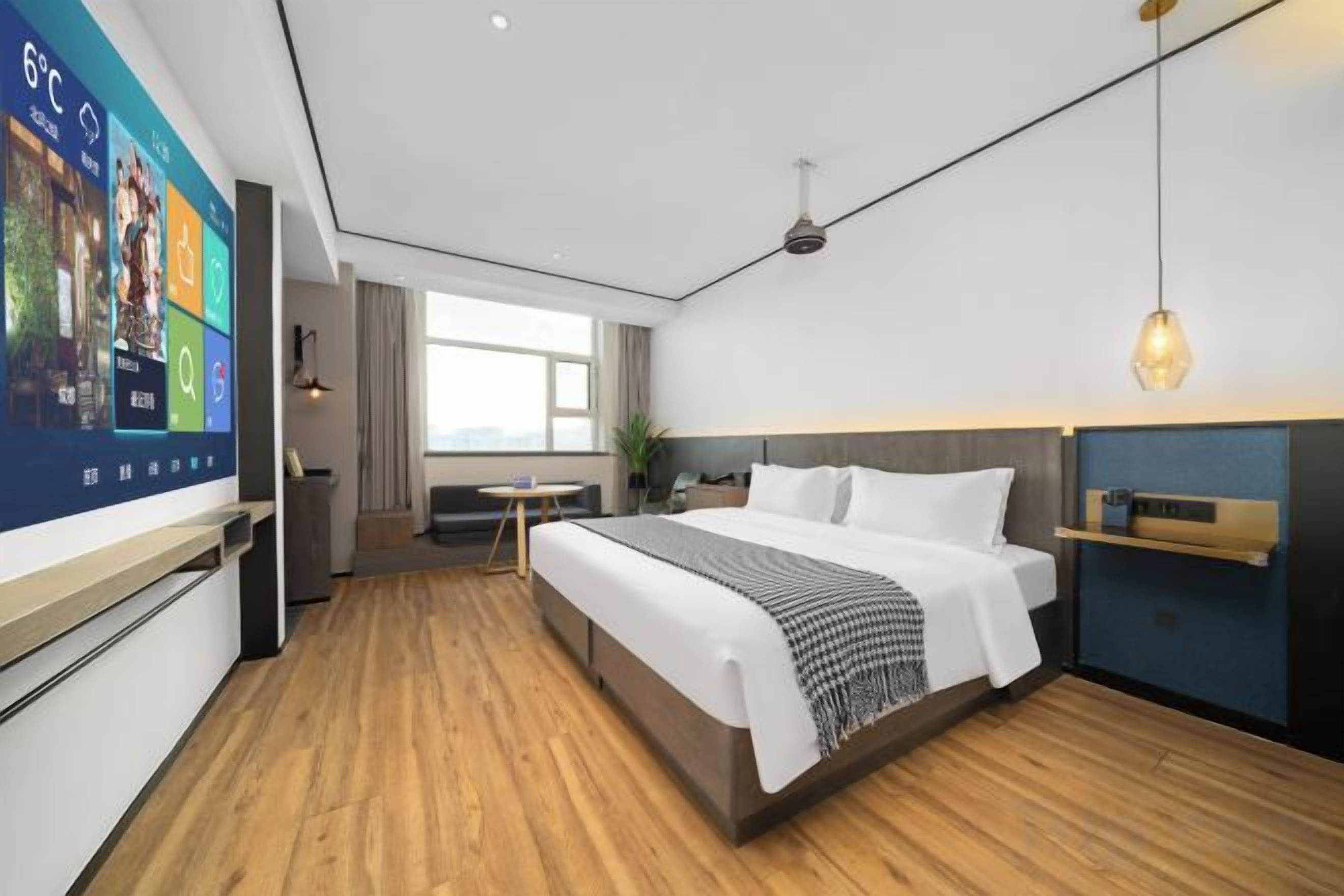 A modern hotel room with a large bed, a desk, and a TV displaying a weather forecast.