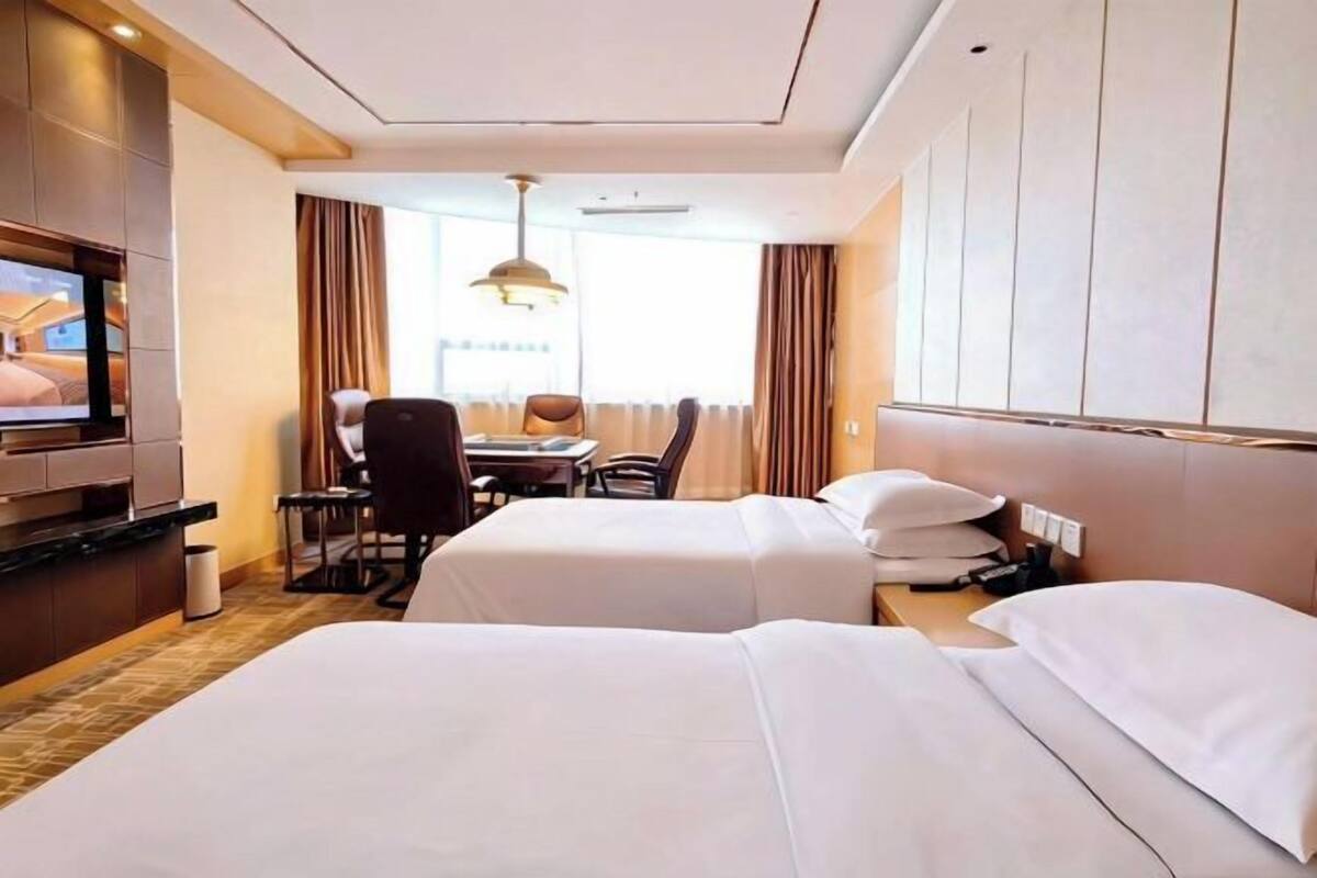 A hotel room with two beds, a desk, a chair, a television, and a window with curtains.