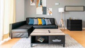A modern living room with a black sofa, colorful cushions, a wooden coffee table, and abstract wall art.