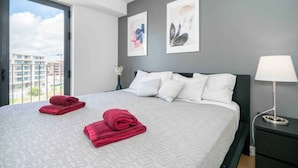 A hotel room with a large bed, grey walls, and two framed artworks.