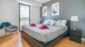 A modern bedroom with a bed, a chair, a nightstand, and artwork on the wall.