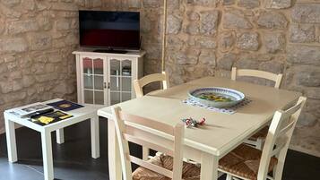 Un comedor con pared de piedra, un televisor sobre un mueble y una mesa servida con platos y un mantel individual.
