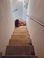 Una scala con corrimano, una persona seduta sugli scalini e un muro con un quadro.