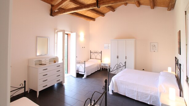 A bedroom with a wooden ceiling, a white dresser, a bed, a nightstand, and a wardrobe. - Reusia Holiday Home (Ragusa)