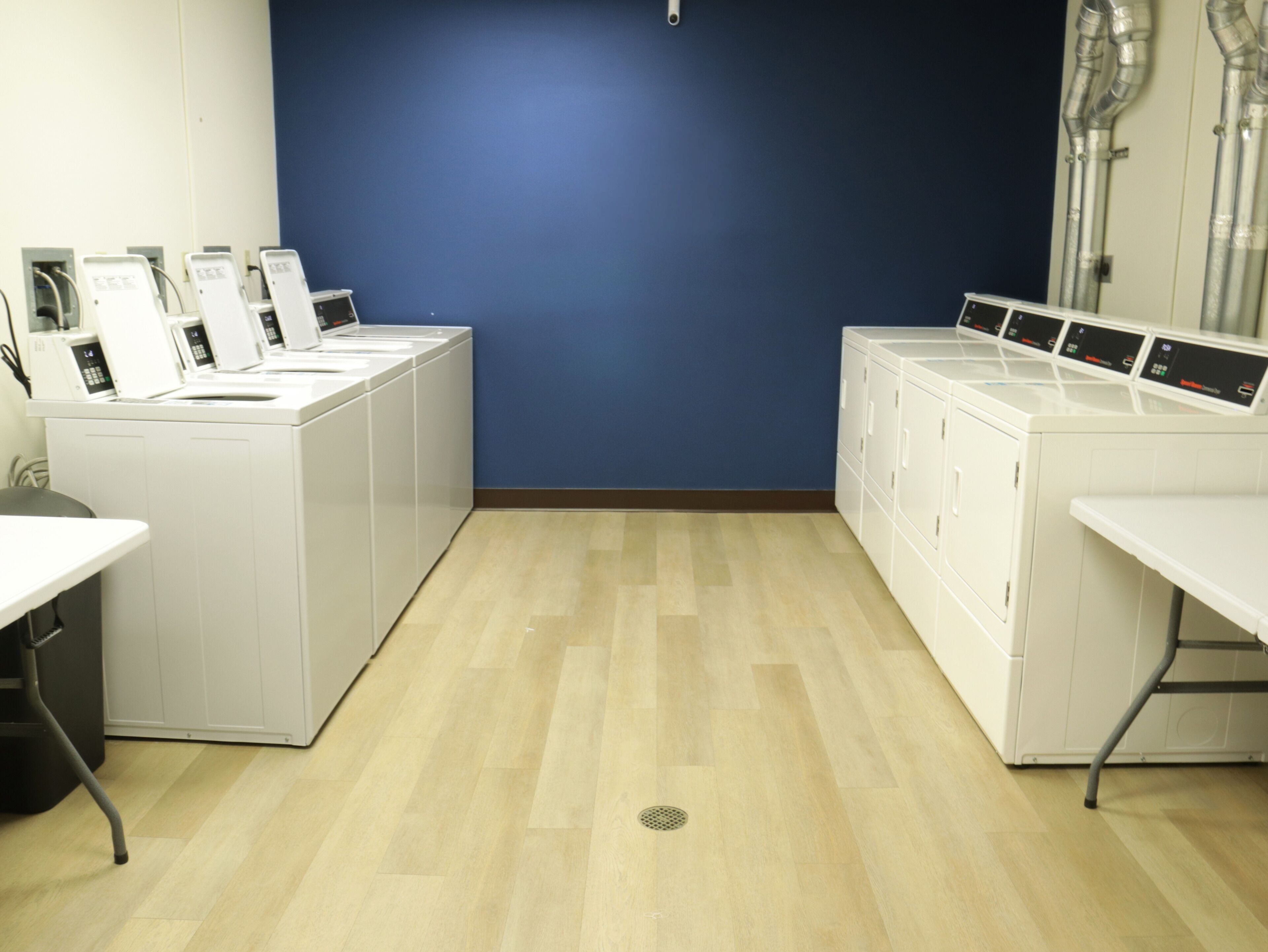 Una sala de lavandería con lavadoras y secadoras blancas, una pared azul y piso de madera.