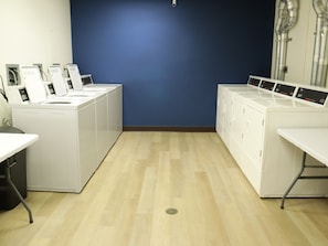 A laundry room with white washers and dryers, a blue wall, and a wooden floor. - Brewster Hall (Cheney)