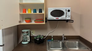 A compact kitchenette with a microwave, coffee maker, and double sink. - Brewster Hall (Cheney)