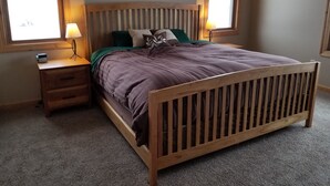 Un dormitorio con una cama de madera, dos mesitas de noche, una mesita auxiliar, una lámpara y dos cuadros enmarcados en la pared.