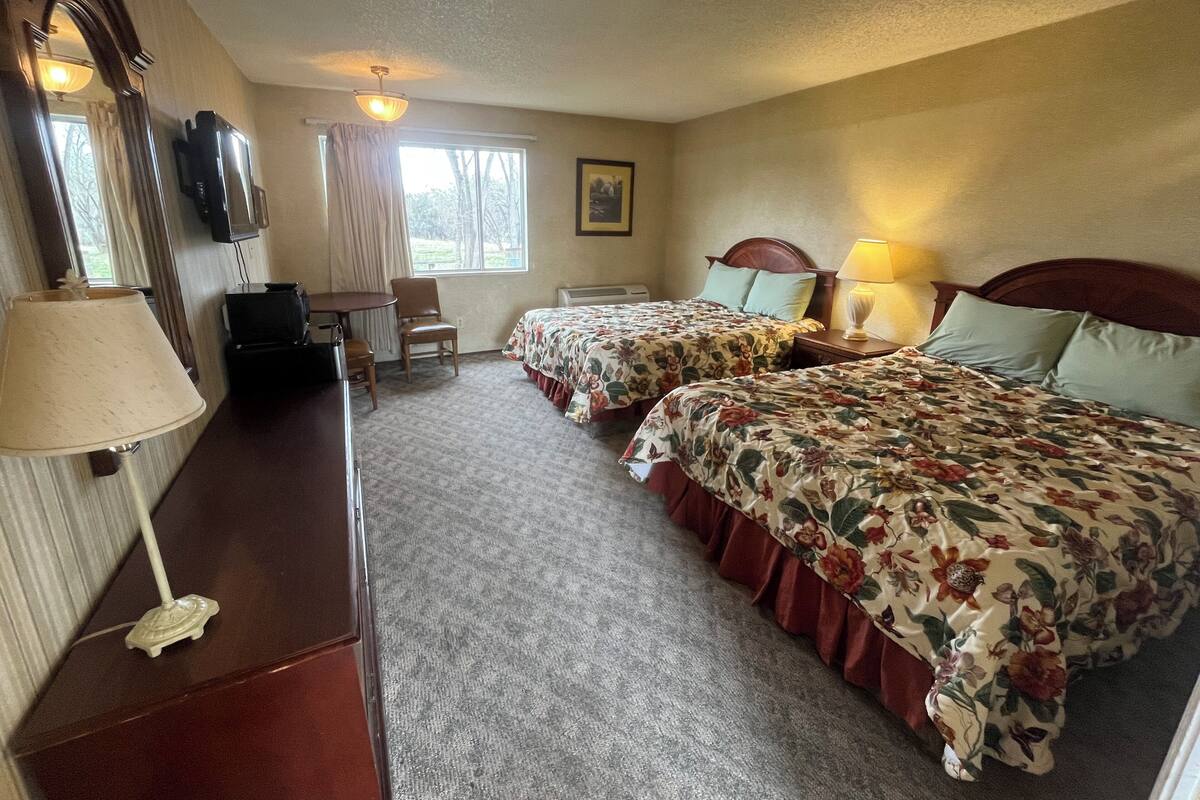 A hotel room with two beds, a desk, a chair, a TV, and a window with curtains.