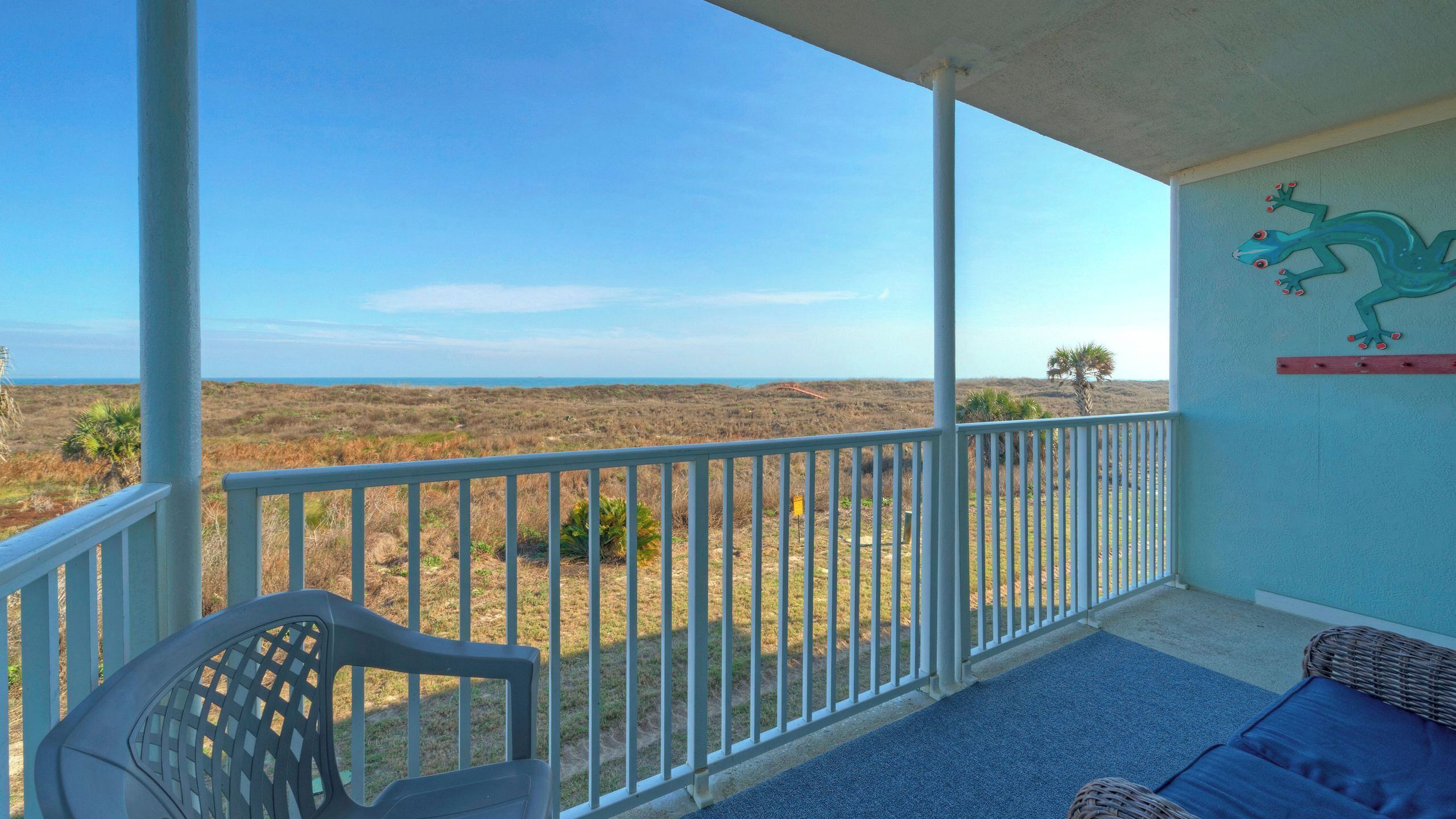 A balcony with a view of the beach, a chair, and a wall decoration.