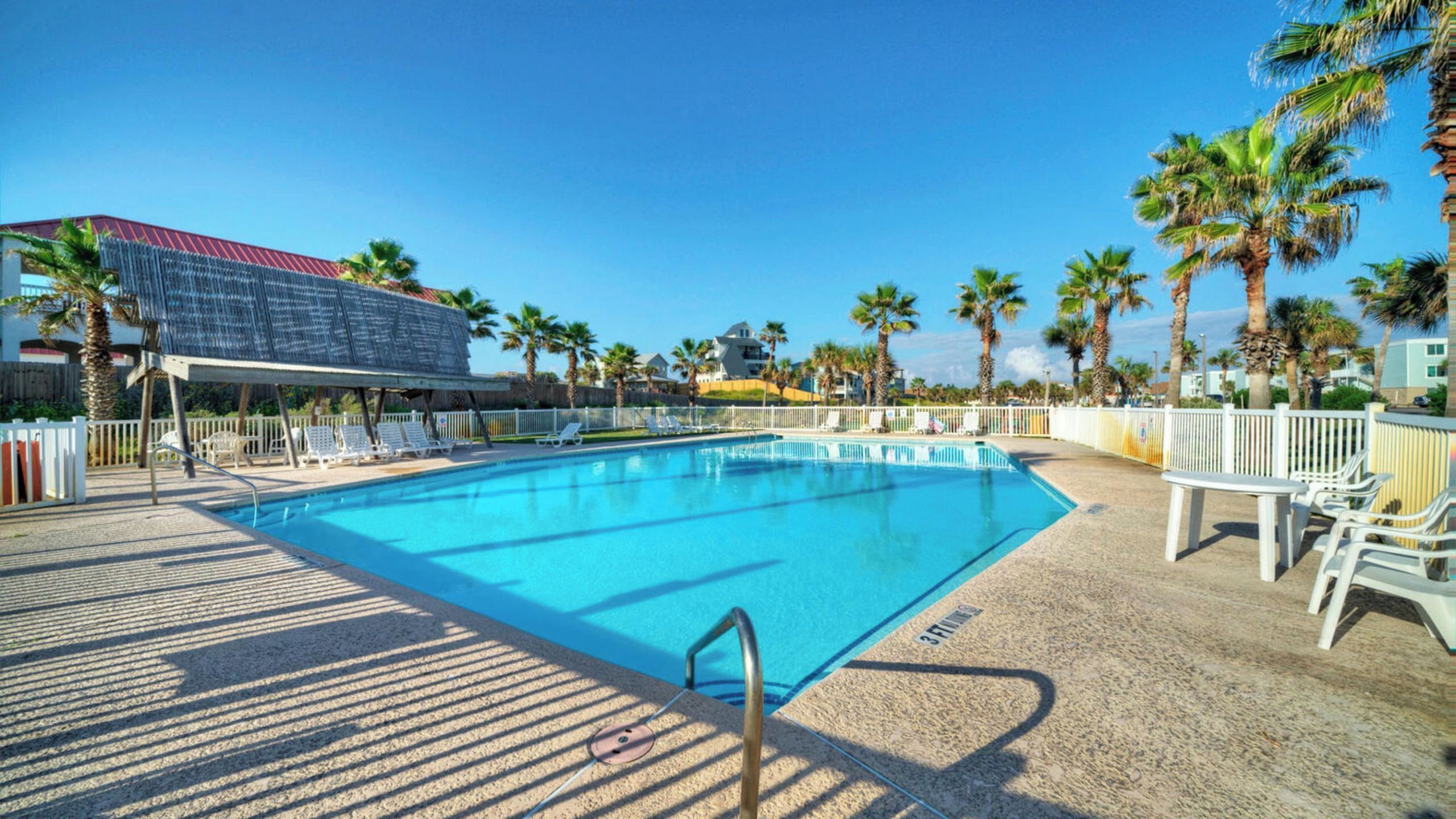 A swimming pool with lounge chairs, palm trees, and a building with a red roof.