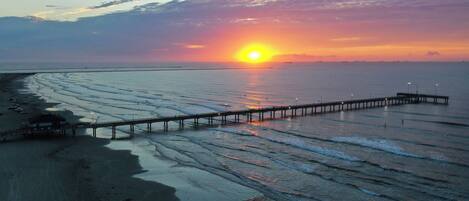 A pier extending into calm waters with a sunset in the background.