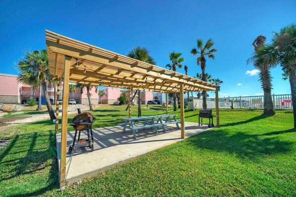 A covered outdoor area with picnic tables and a barbecue grill. - Beachfront Condo w/ Ocean View, 2 Pools, Boardwalk to the Beach Island Getaway (Port Aransas)