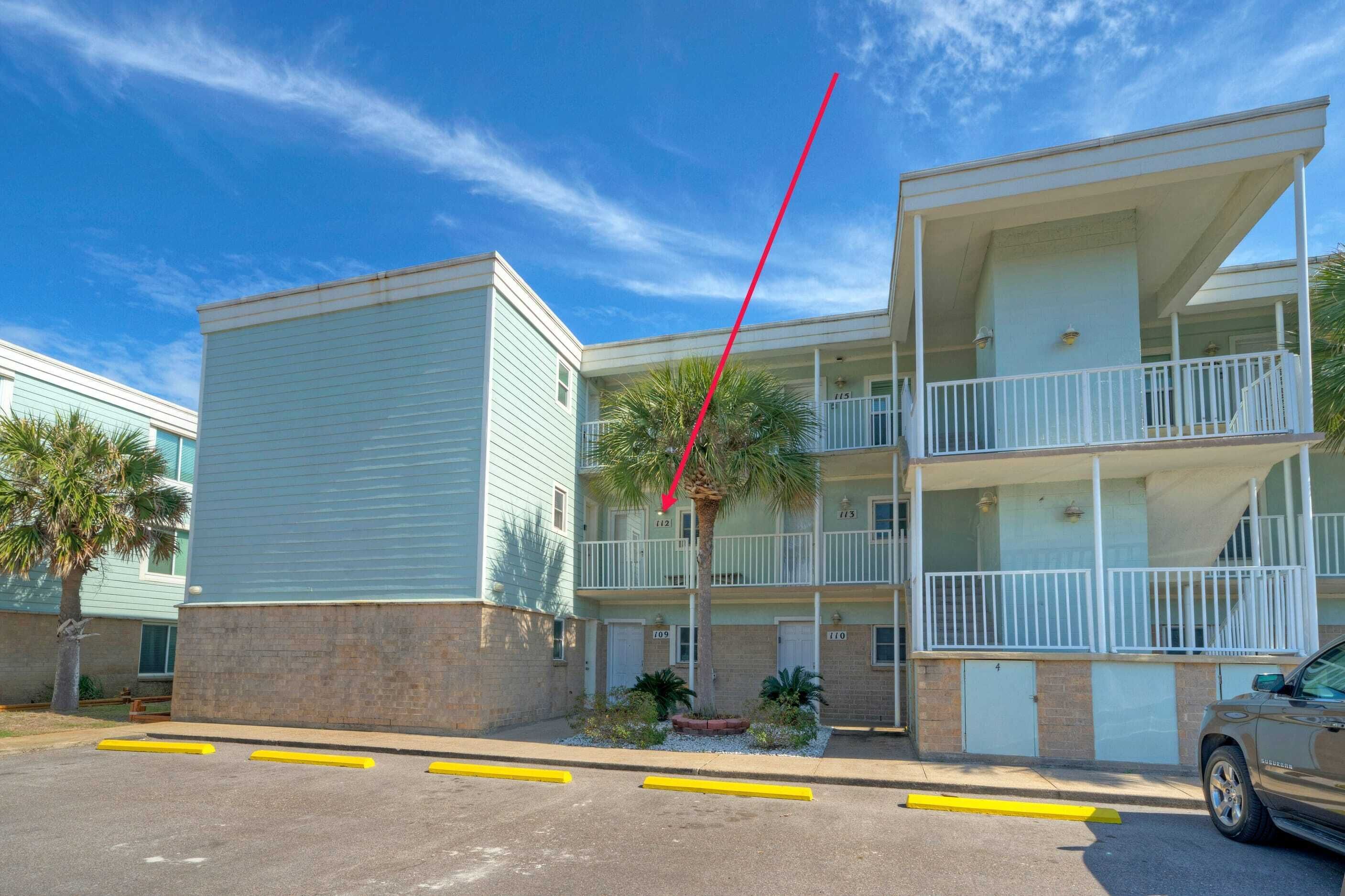 A two-story building with a light blue exterior, a balcony on the second floor, and a palm tree in the courtyard.