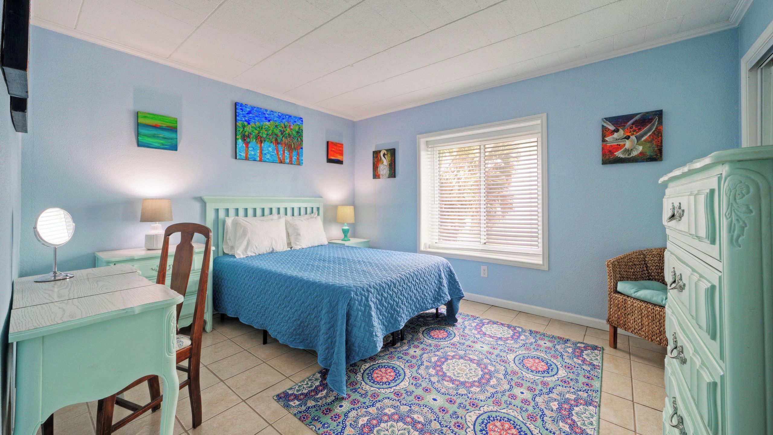 Une chambre à coucher comprenant un lit, une chaise, une commode, une lampe et une fenêtre avec des stores.