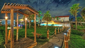 A wooden pergola, a pool, and a building with a red roof. - Beachfront Condo w/ Ocean View, 2 Pools, Boardwalk to the Beach Island Getaway (Port Aransas)