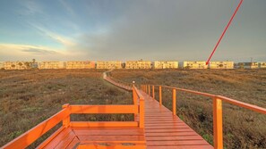 A wooden boardwalk leading to a row of buildings with a clear sky above. - Beachfront Condo w/ Ocean View, 2 Pools, Boardwalk to the Beach Island Getaway (Port Aransas)