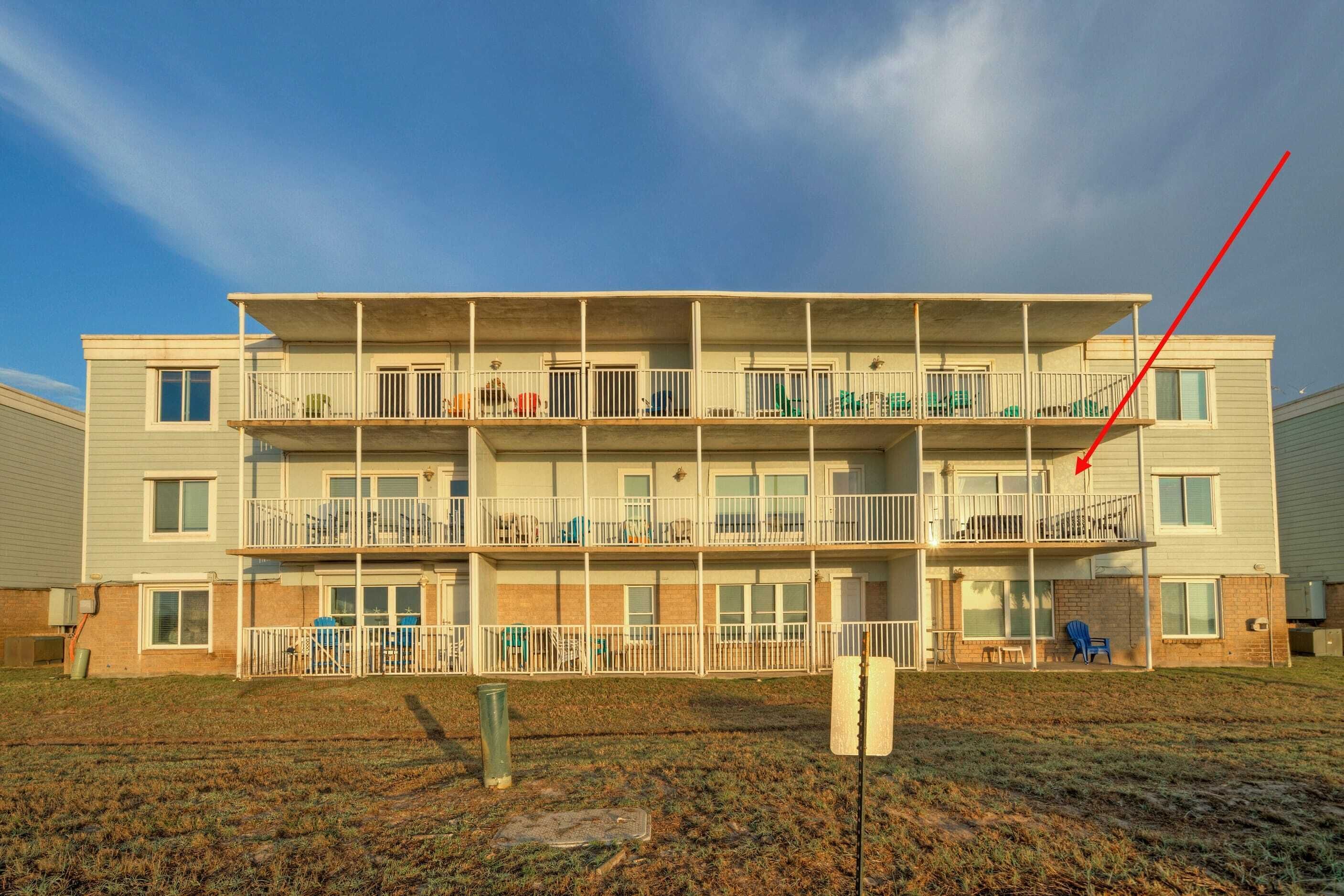 A multi-story apartment building with balconies, a grassy yard, and a clear sky.
