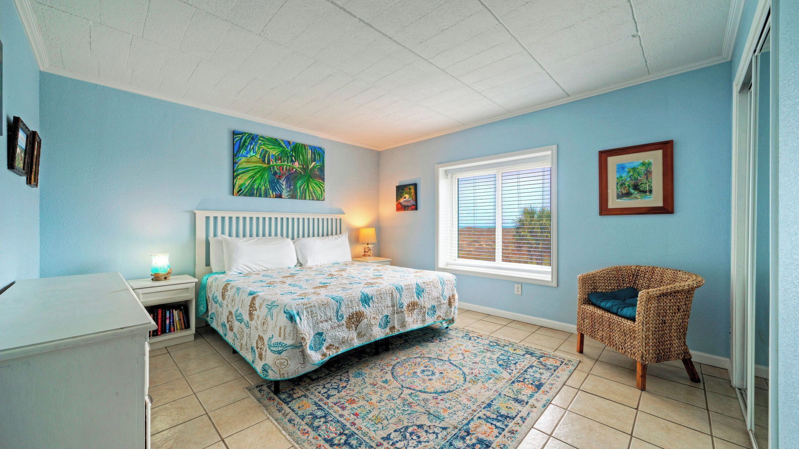 A bedroom with a bed, a chair, a nightstand, a window, and a painting on the wall.