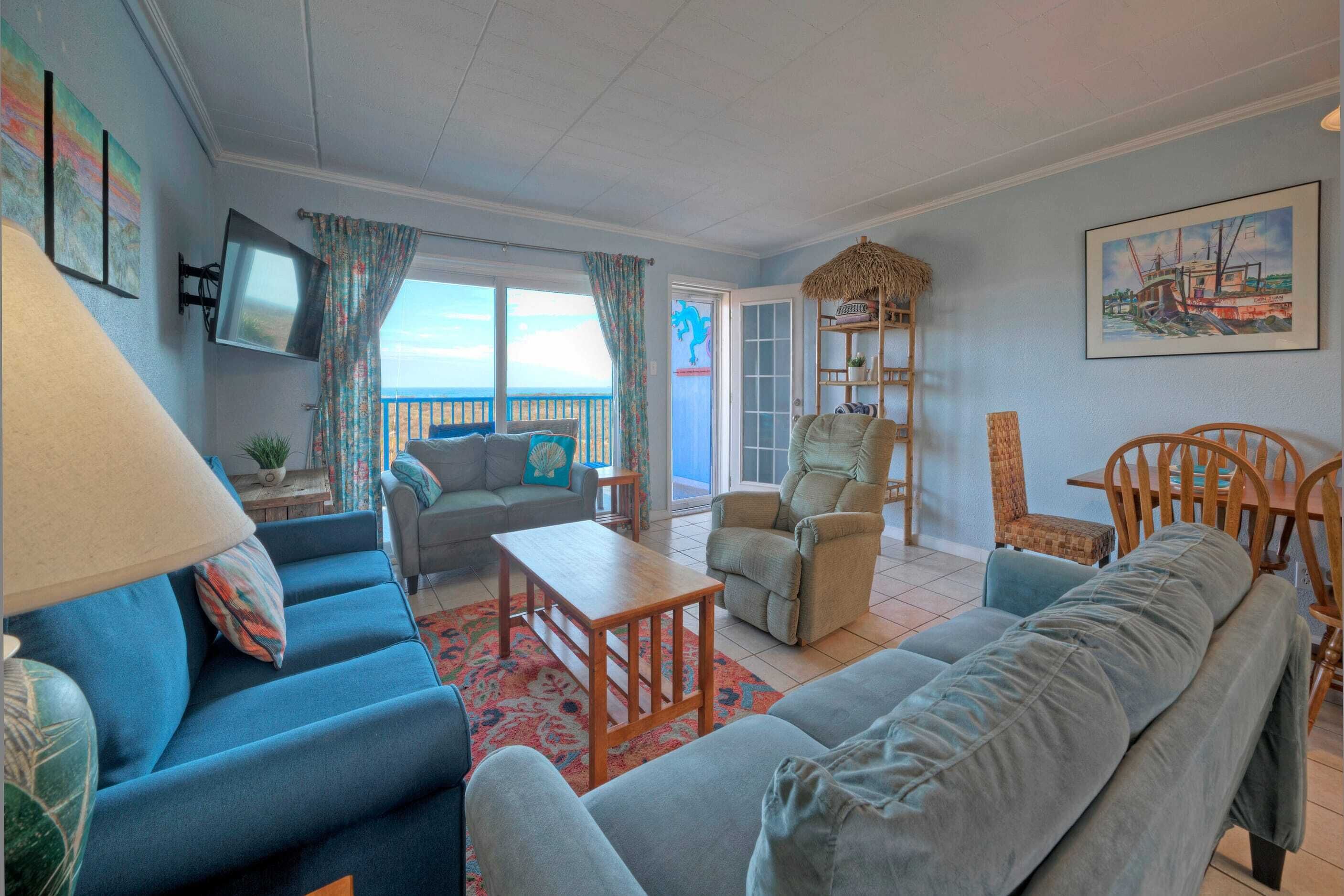 A living room with a sofa, armchair, and coffee table, a television, and a view of the outdoors.
