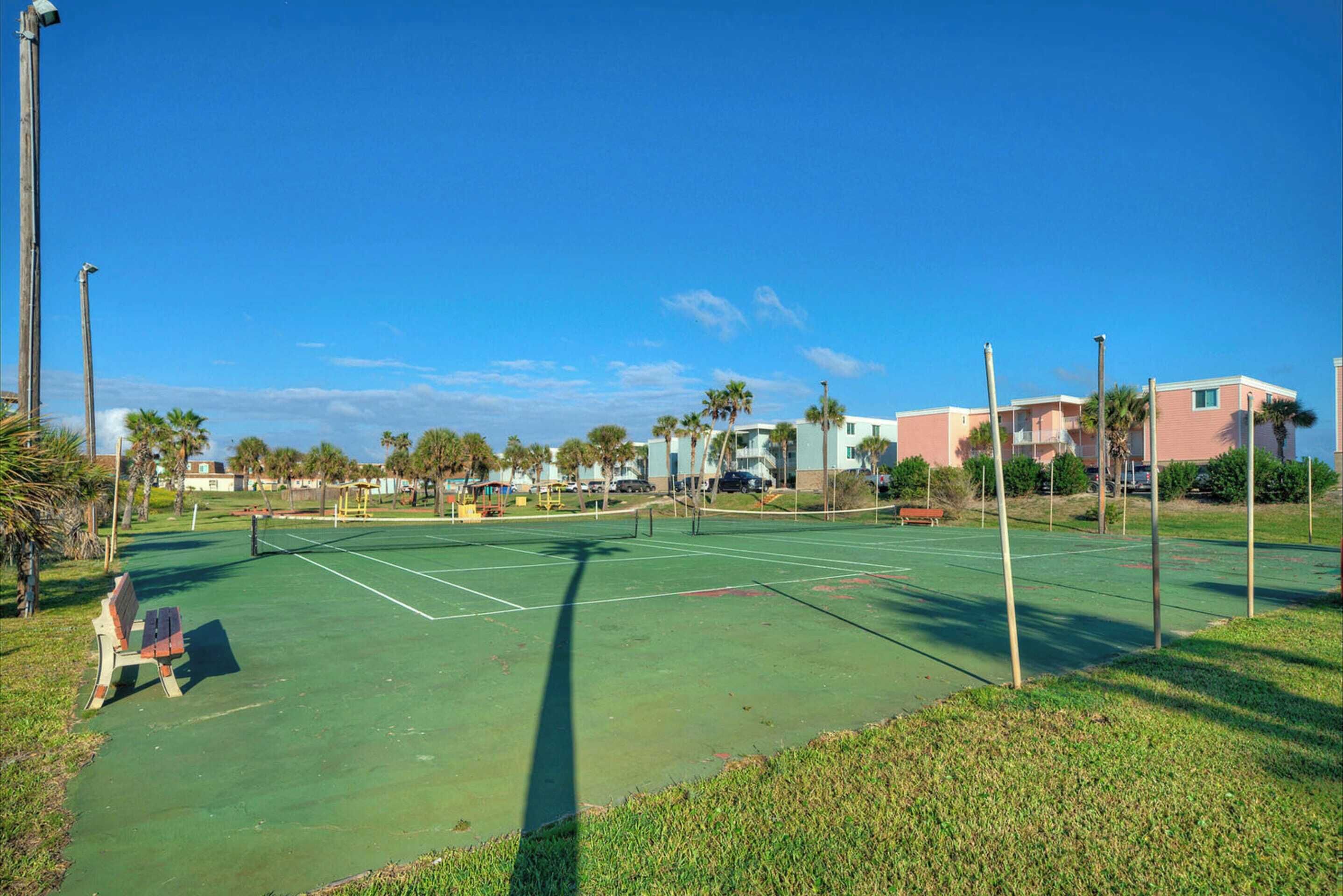 A tennis court with a net, benches, and palm trees.