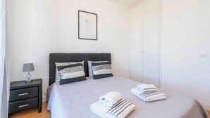 Un lit bien fait, avec une couvre-lit grise et deux serviettes pliées posées sur le côté.