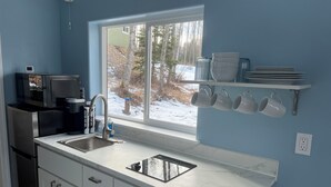 A modern kitchen with a sink, a microwave, a coffee maker, and a window with a view of a snowy landscape.