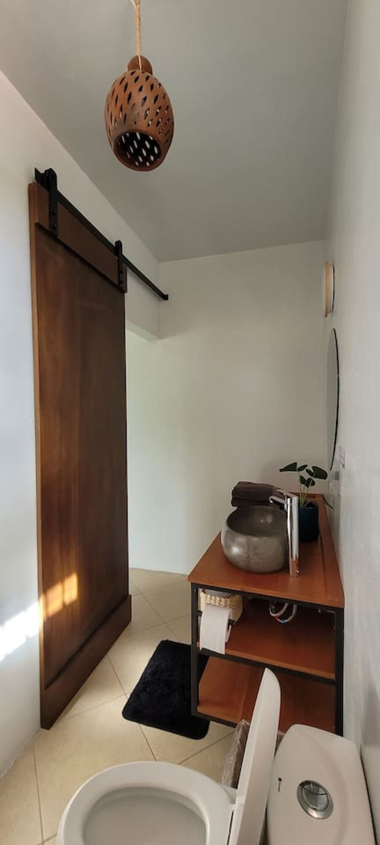Un baño pequeño con inodoro, lavabo y una lámpara colgante, además de una puerta de madera.