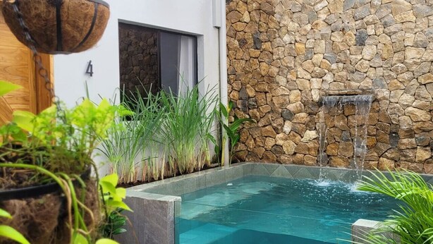 Une piscine bordée d’un mur en pierre et agrémentée d’une petite cascade, le tout entouré de différentes espèces de plantes.