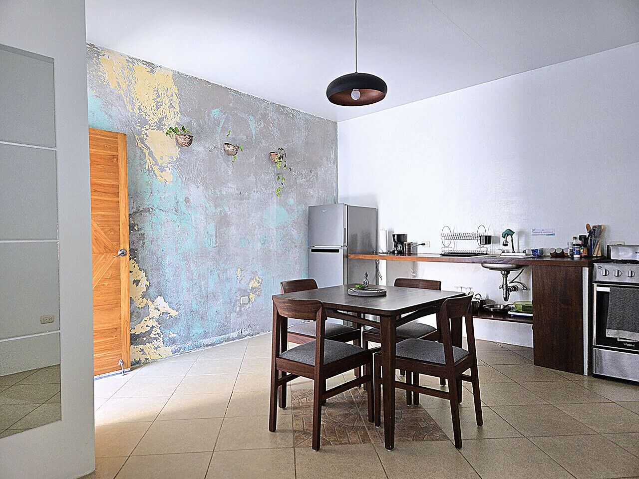 A compact kitchen with a dining area, a wooden door, and a wall with a distressed paint finish.