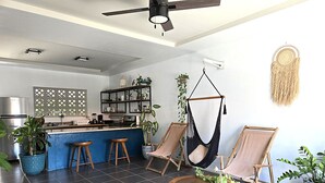 Une cuisine moderne avec un coin bar, deux chaises en bois, un fauteuil suspendu et une table ronde en bois agrémentée de plantes.
