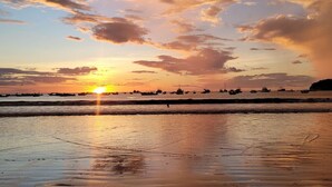 Une plage au coucher du soleil, avec des bateaux sur l’eau et un ciel dégagé.